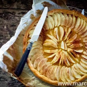 Tarte aux pommes artisanale avec couteau, sur papier cuisson.