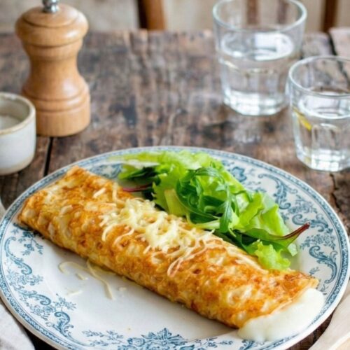 Crêpe farcie au fromage, salade, sur table en bois.