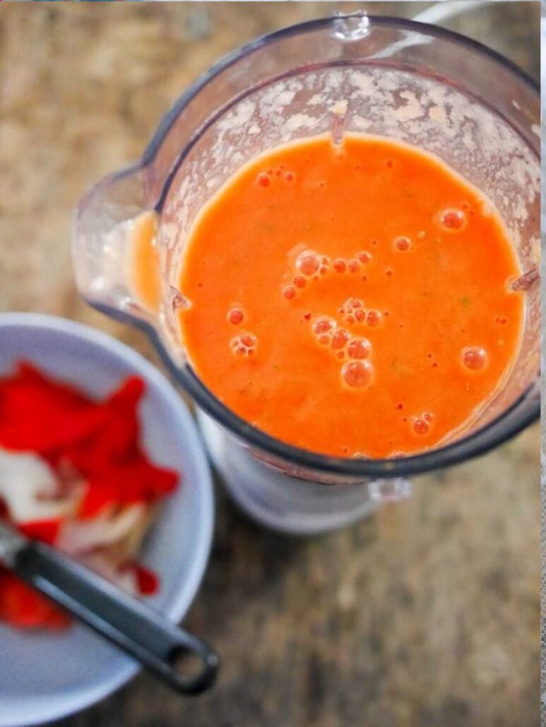 Smoothie orange dans un mixeur, ingrédients à côté.
