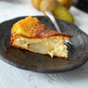 Part de gâteau aux poires caramélisées sur assiette noire.
