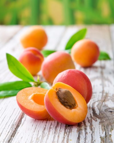 Abricots frais avec feuilles sur table en bois.
