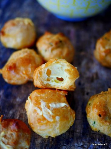 Gougères au fromage, coupées, sur planche en bois.
