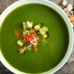 Soupe verte, croûtons et garnitures rouges dans un bol.