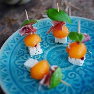 Brochettes melon, jambon cru, feta, basilic sur assiette