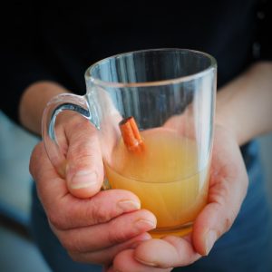 Mains tenant un verre de cidre chaud à la cannelle.