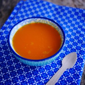 Bol de soupe orange sur tissu bleu, cuillère bois