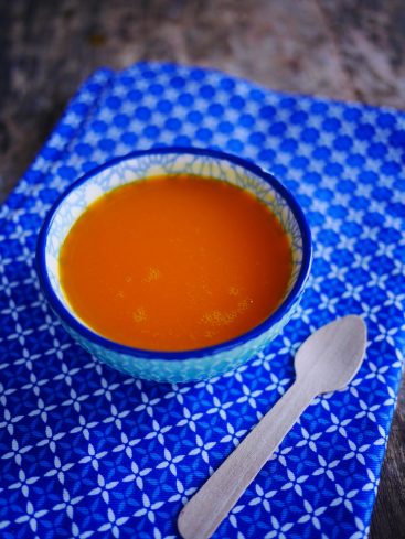 Bol de soupe orange sur tissu bleu, cuillère bois