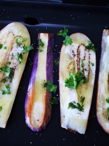Aubergines grillées avec herbes et sel sur une plaque.
