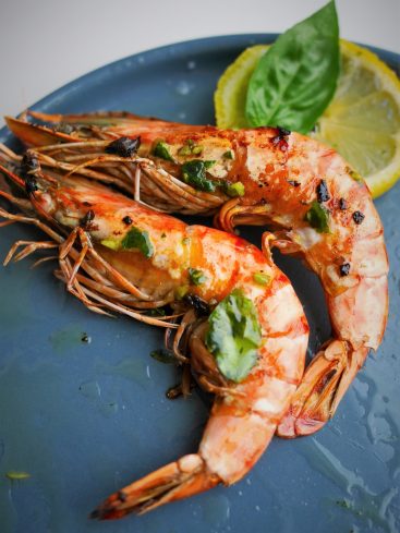 Gambas grillées avec citron et basilic sur assiette.