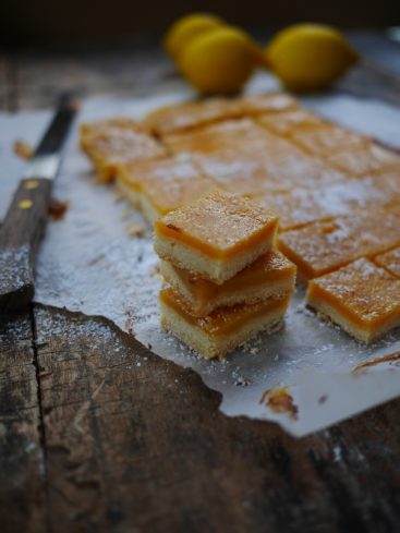 Carrés au citron saupoudrés de sucre glace sur bois.