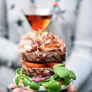 Double burger gourmand tenu à la main, cocktail