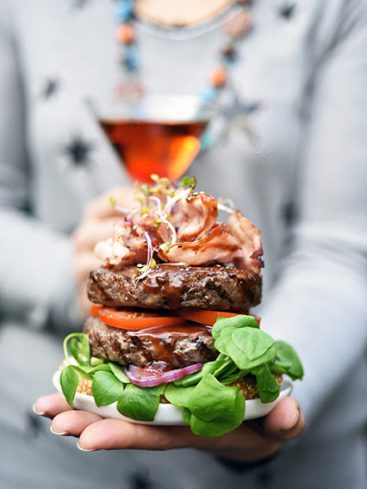 Double burger gourmand tenu à la main, cocktail