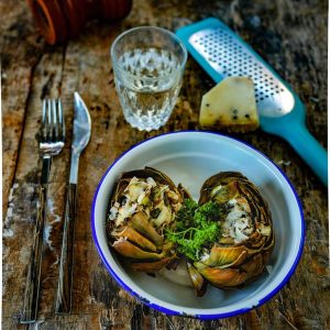 Artichauts farcis, fromage, verre d'eau sur table en bois.