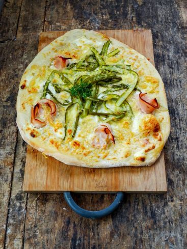 Pizza aux asperges et jambon sur planche en bois.