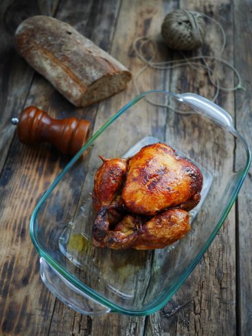 Poulet rôti, pain, moulin à poivre sur table rustique.