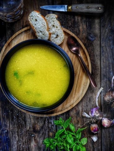 Assiette de soupe, pain, ail et menthe sur bois.