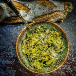 Baguette et plat de courgettes sautées avec une cuillère.