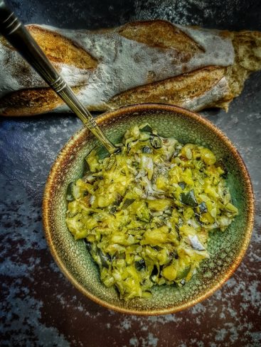 Baguette et plat de courgettes sautées avec une cuillère.