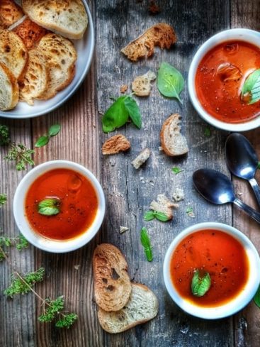 Soupe tomate maison, croûtons et basilic frais sur bois.