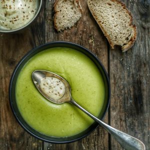 Velouté vert, crème et pain sur table en bois