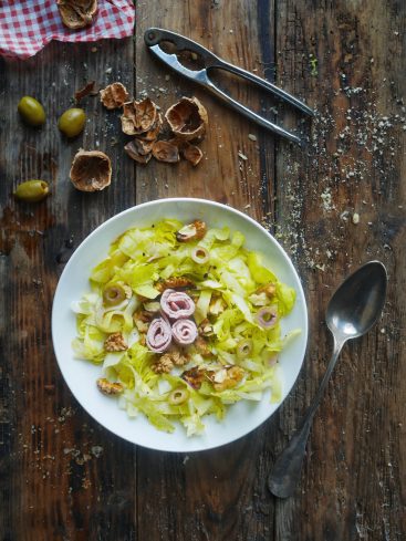 Salade de laitue, noix et jambon sur table en bois.