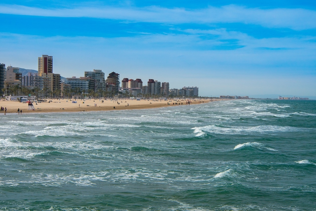 Plage ensoleillée avec immeubles et mer agitée.
