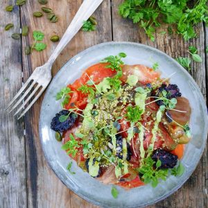 Salade de tomates colorées, mûres et sauce verte sur bois