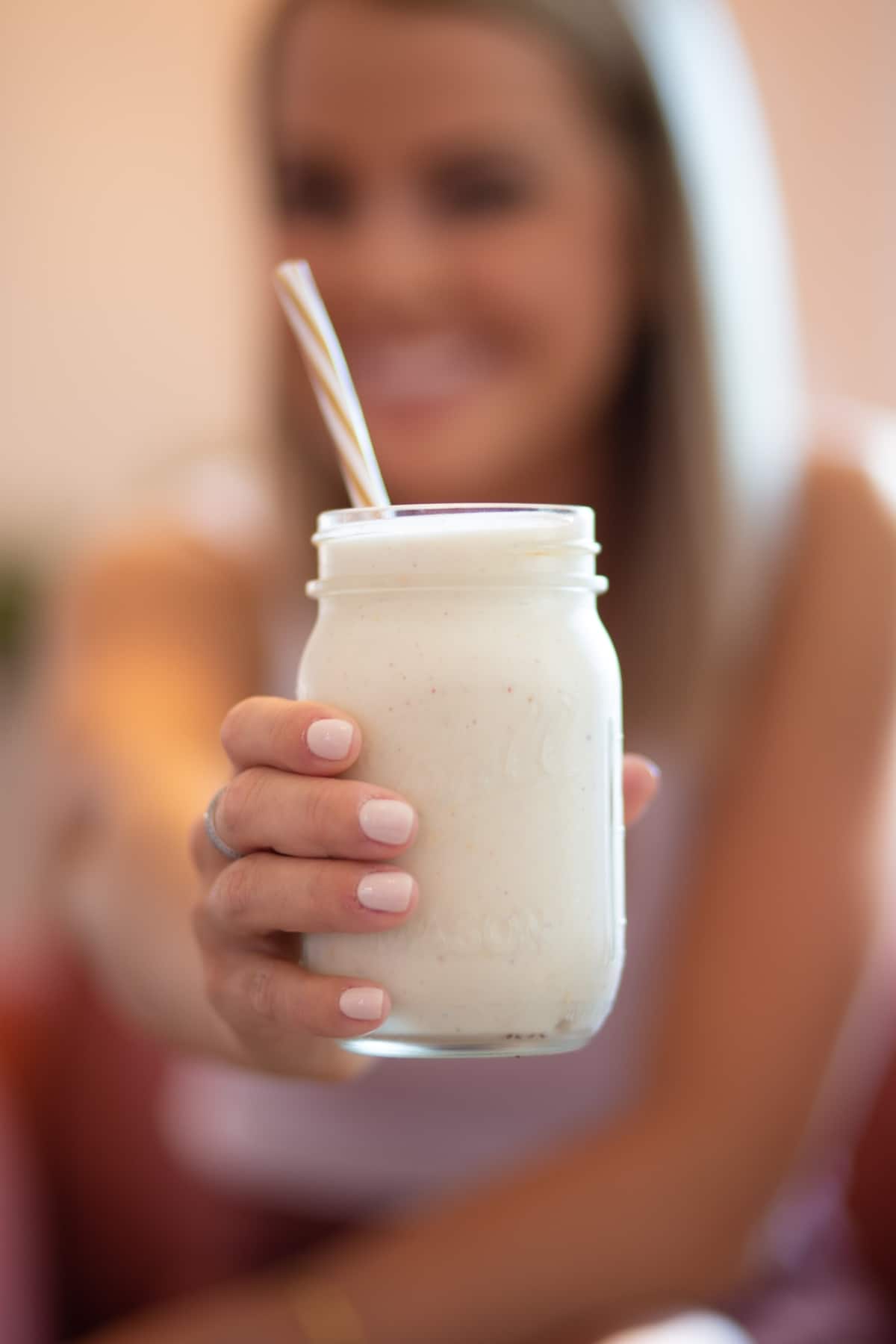 Femme tenant un smoothie blanc dans un bocal.