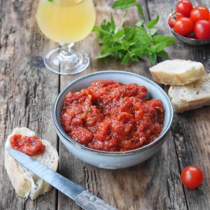 Ajvar, pain, tomates et boisson sur table en bois.