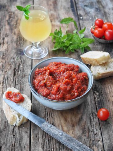 Ajvar, pain, tomates et boisson sur table en bois.