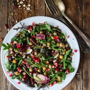 Salade de légumineuses colorée avec grenade sur table en bois.