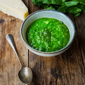 Bol de pesto, parmesan et épinards sur bois rustique.