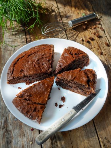 Gâteau au chocolat coupé, sur assiette blanche, table bois.