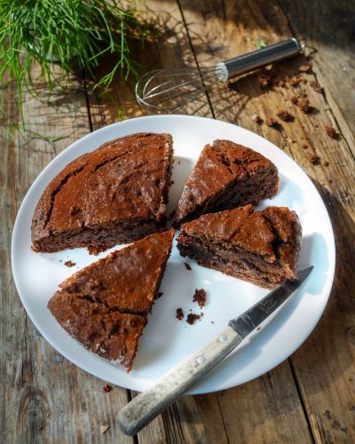 Gâteau au chocolat coupé, sur assiette blanche, table bois.