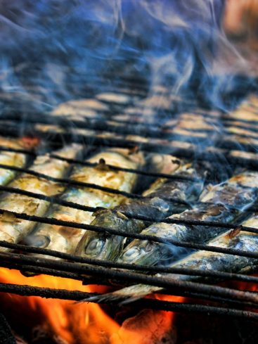 Sardines grillées sur un barbecue, fumée et flammes.