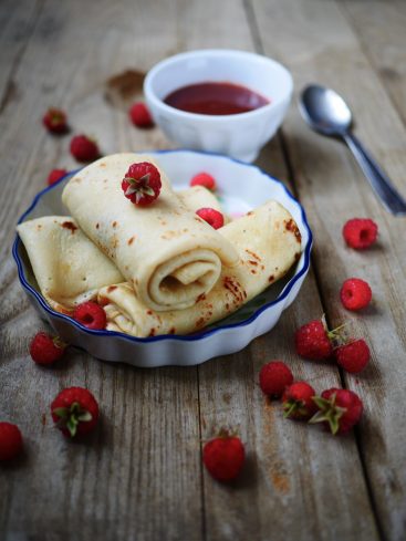 Crêpes roulées aux framboises et sauce, sur table en bois