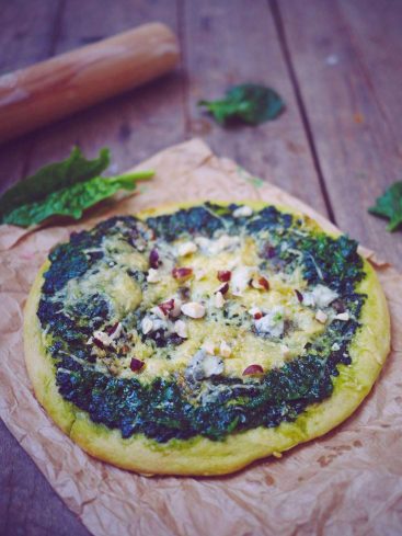 Pizza épinards, fromage et noisettes sur table en bois.