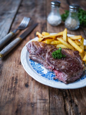 Steak frites sur assiette bleue, table en bois.