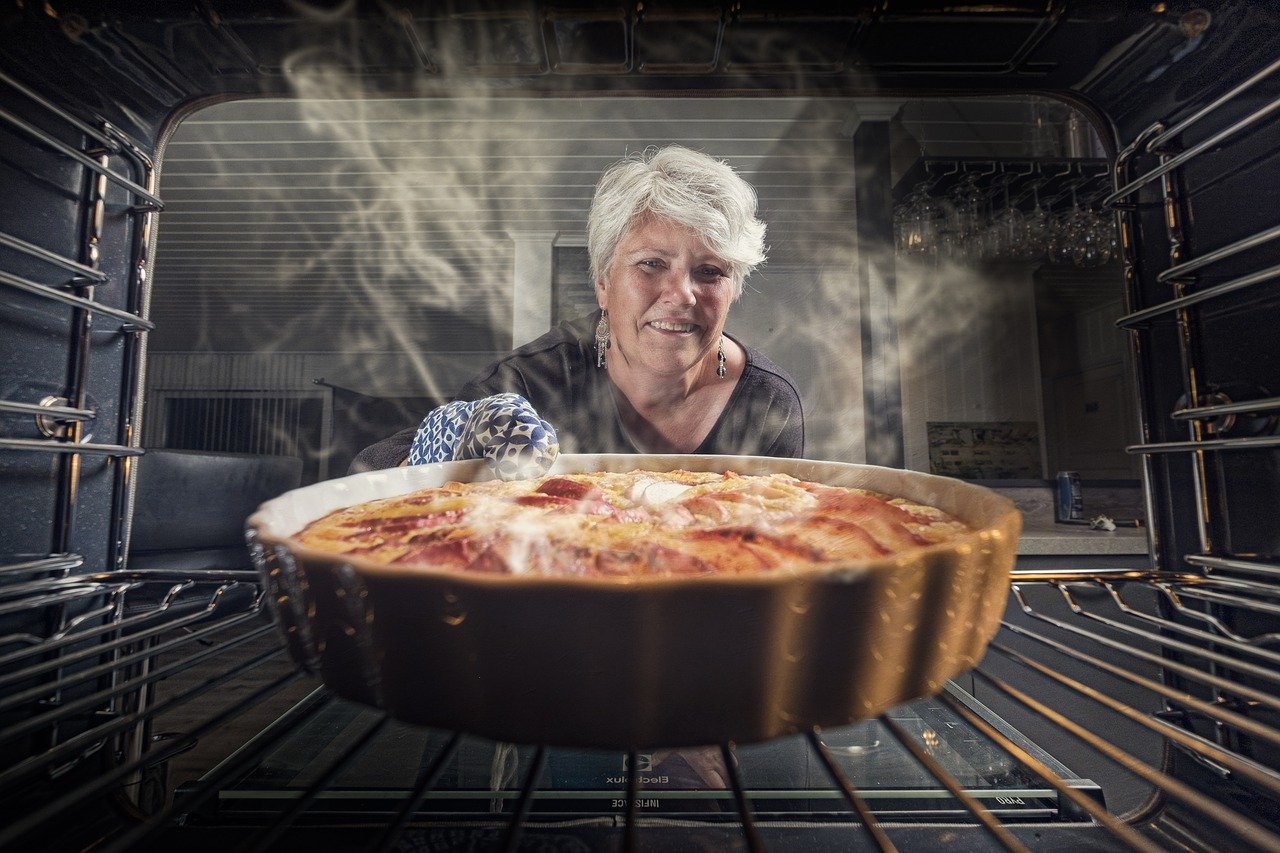 Femme souriante sortant un gratin fumant du four.