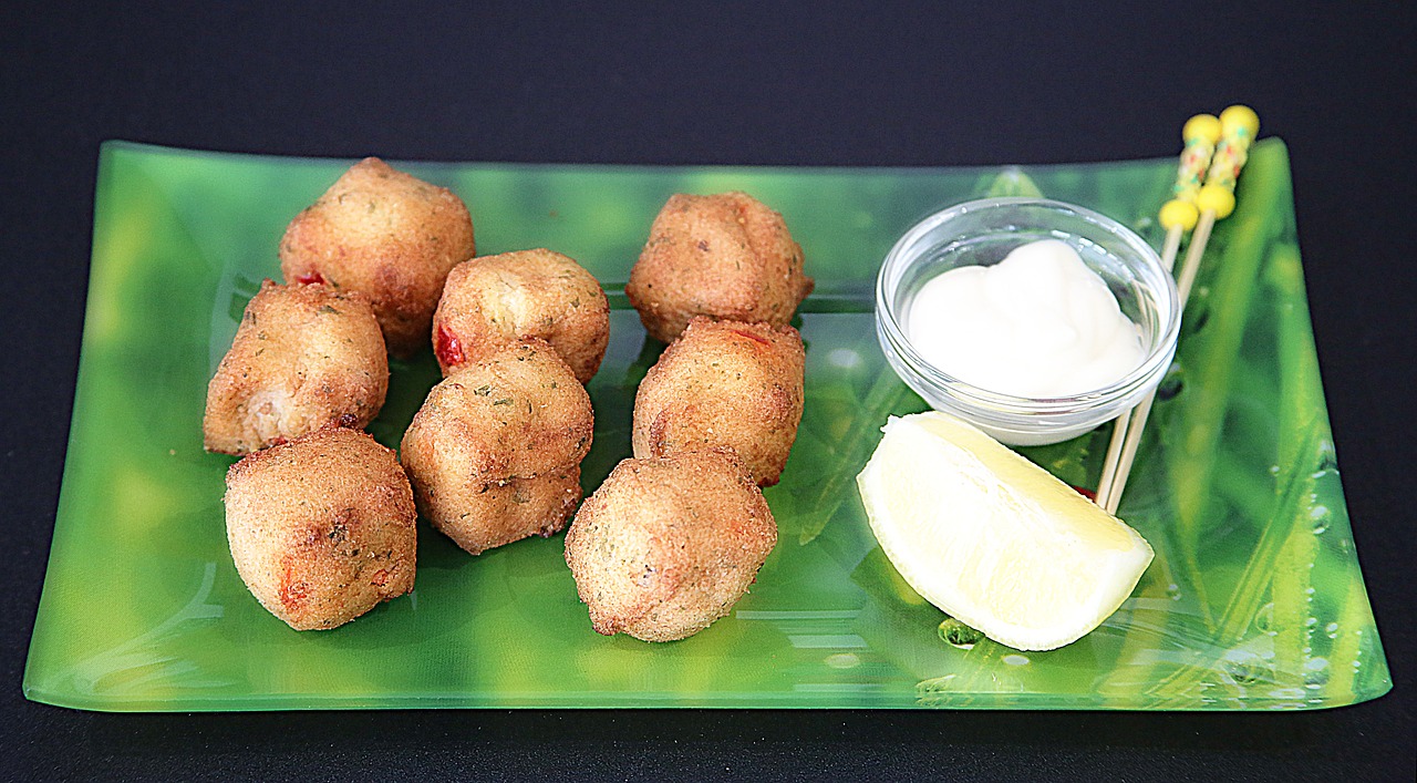 Accras de morue avec sauce et citron sur plateau.