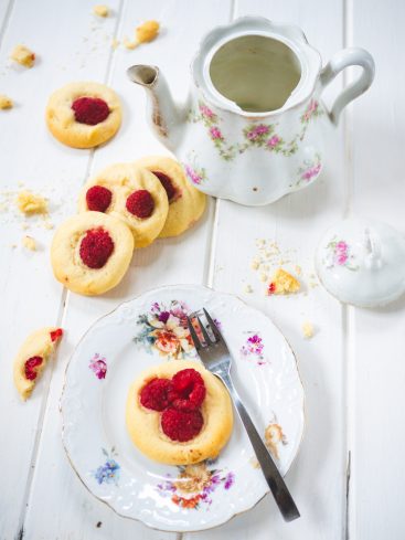 Théière, biscuits aux framboises sur table blanche