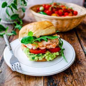 Burger au saumon, avocat et tomates sur table bois.