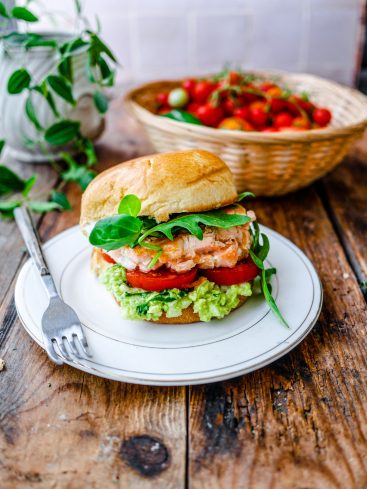Burger au saumon, avocat et tomates sur table bois.