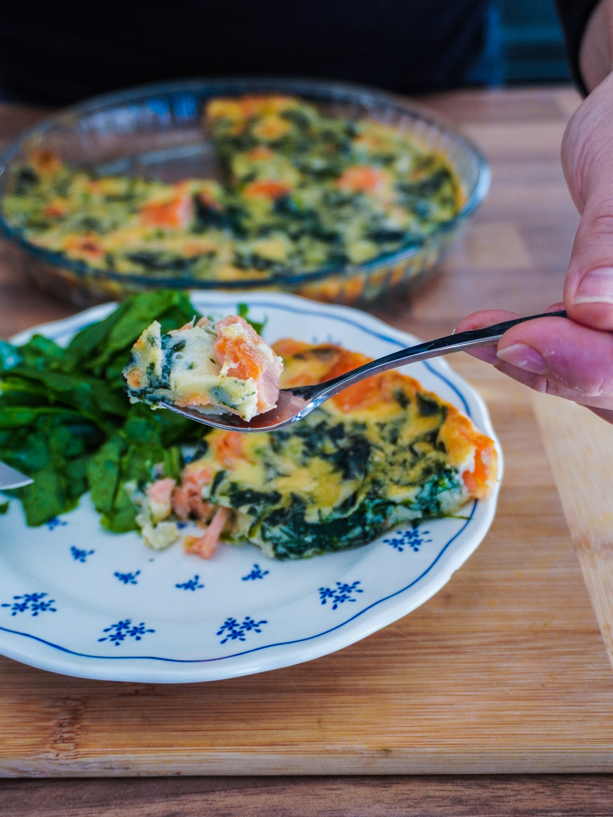 une part de quiche sans pâte epinard saumon tenu dans une fourchette au dessus d'une assiette