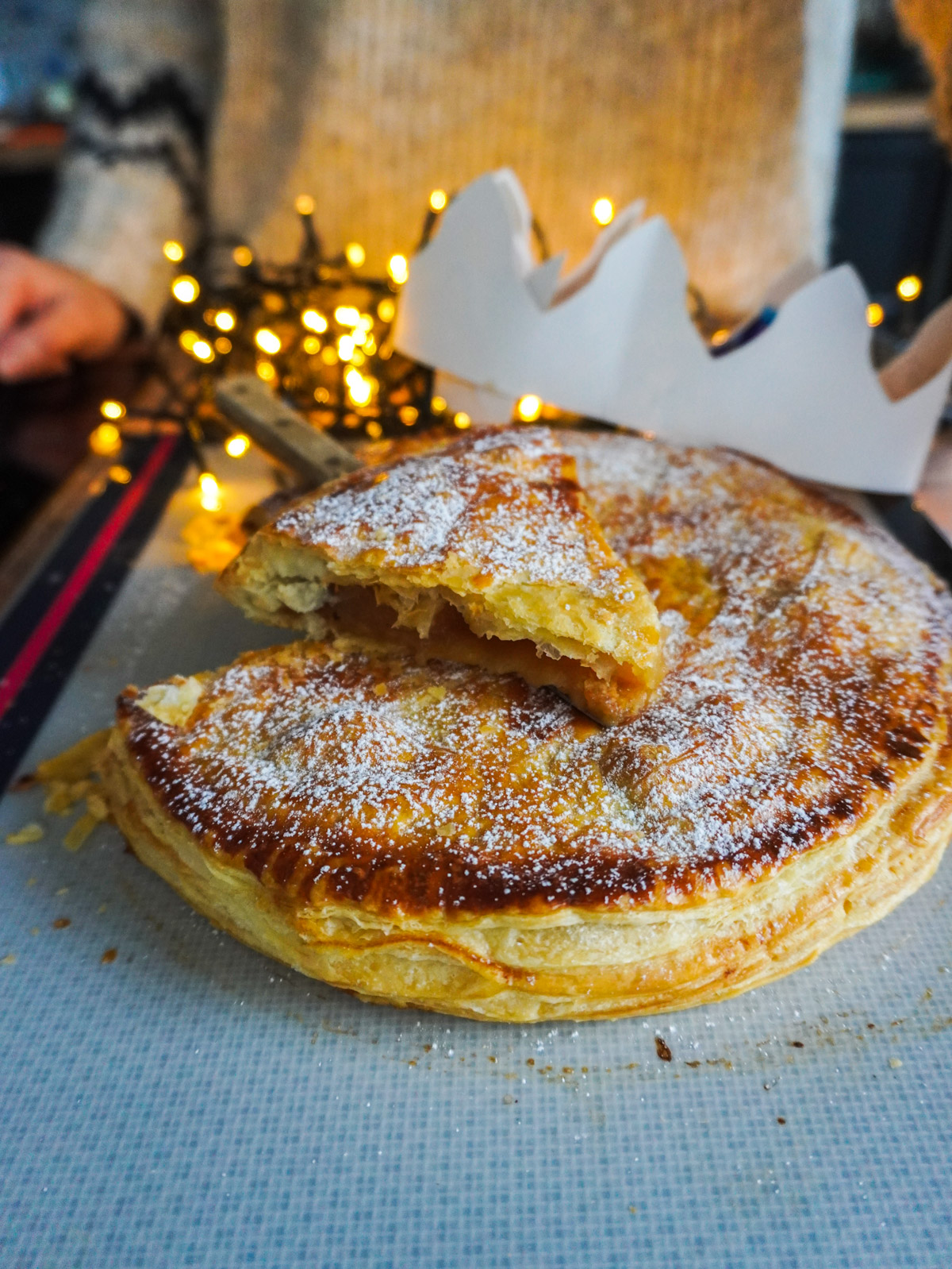 Une part de galette des rois à la pomme découpée, posée sur la galette avec une couronne blanche