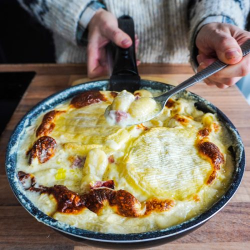Cuillère de gnocchiflette tenue au dessus d'un plat gratiné
