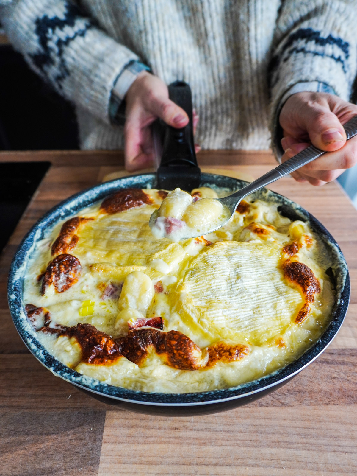 Cuillère de gnocchiflette tenue au dessus d'un plat gratiné