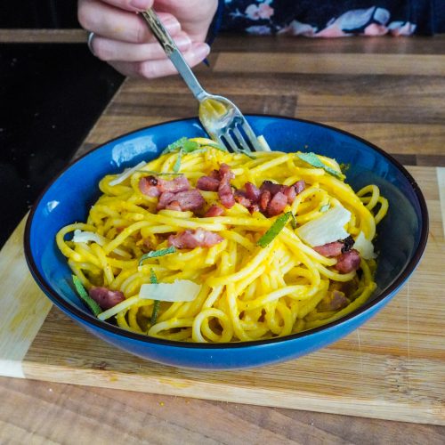 une assiette de spaghettis à la crème de courge et aux lardons grillés, et de copeaux de parmesan, parsemée de feuilles de sauge