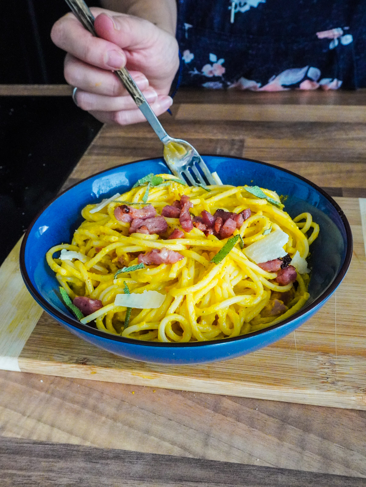 une assiette de spaghettis à la crème de courge et aux lardons grillés, et de copeaux de parmesan, parsemée de feuilles de sauge