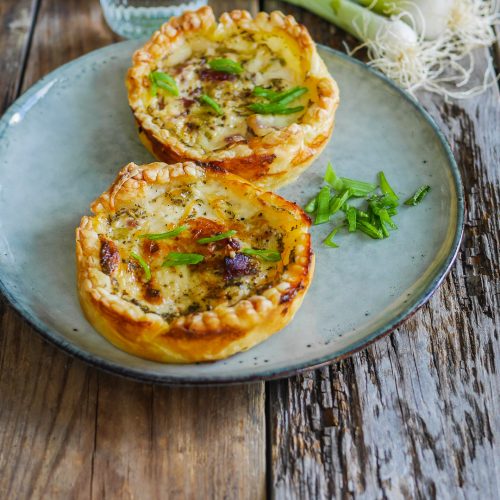 Tartelettes salées, oignons nouveaux, verre d'eau sur bois.